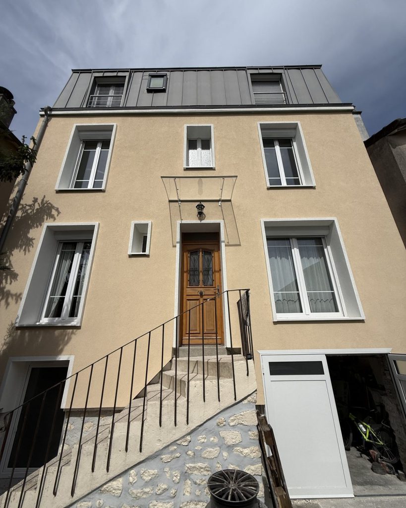 Même façade après isolation thermique par l extérieur, enduit beige uniforme et encadrements repris